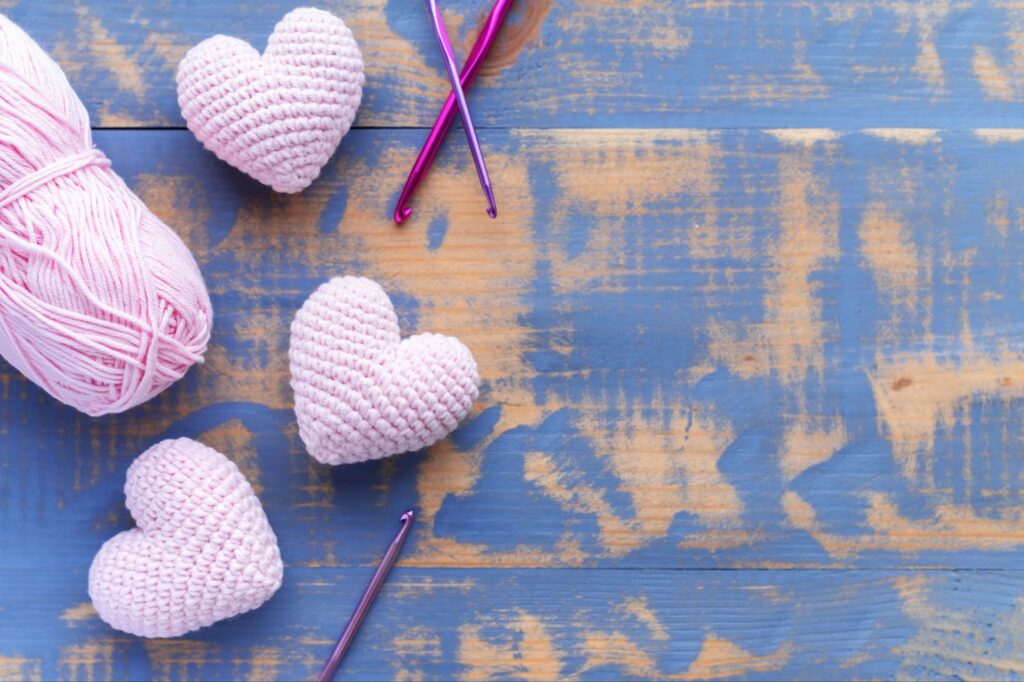 Top view of handmade knitted three pink hearts with ball of yarn