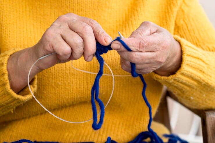 Woman in a Yellow Sweater is Knitting With Blue Yarn