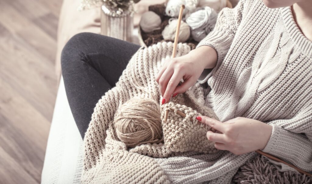 Top view of wooden knitting needles and yarn in woman's hands